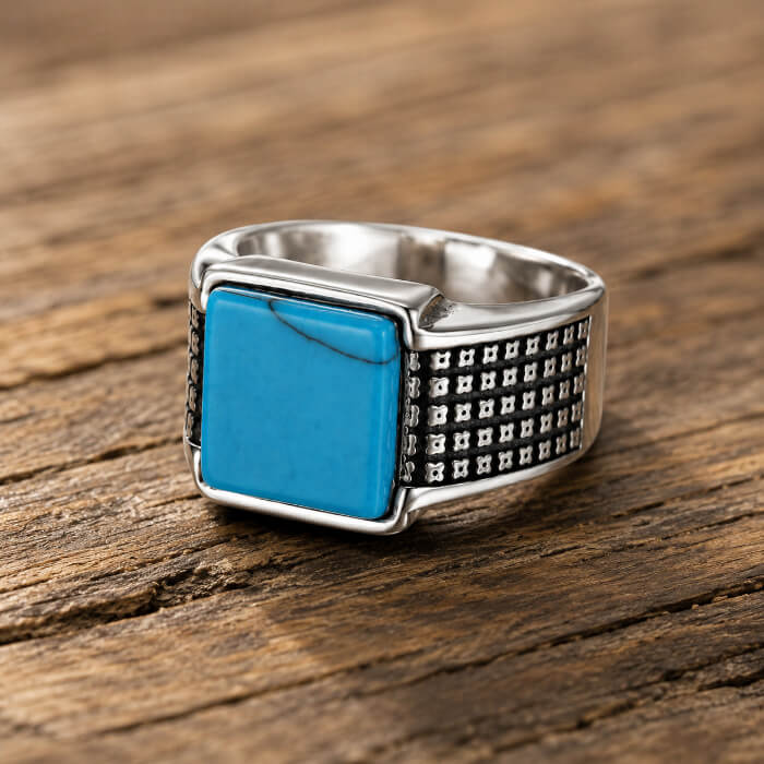 Front view of a square turquoise men's stainless steel ring with geometric textured shoulders