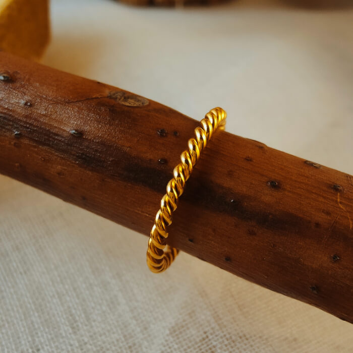 Twisted rose gold band ring resting on a textured wooden branch