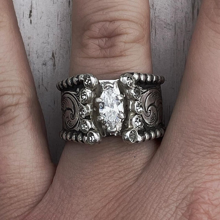 Engagement ring with marquise diamond and ornate silver band on hand