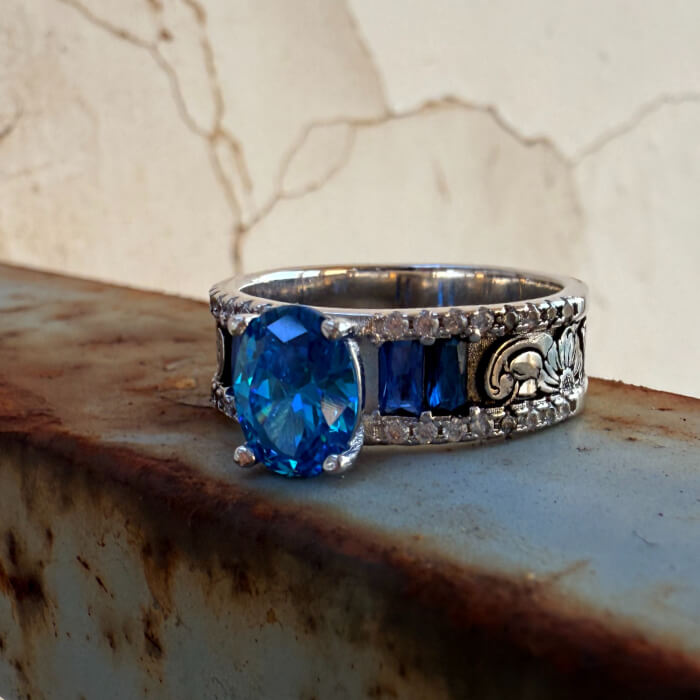 Oval blue sapphire ring with ornate silver band and diamond accents