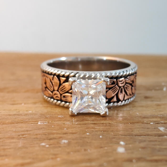 Close-up of rose gold flower engraved ring with a princess cut diamond
