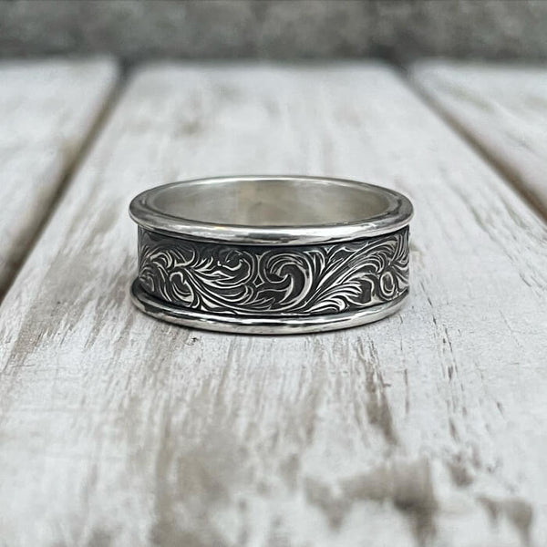 Handcrafted silver ring with floral engravings on wooden background