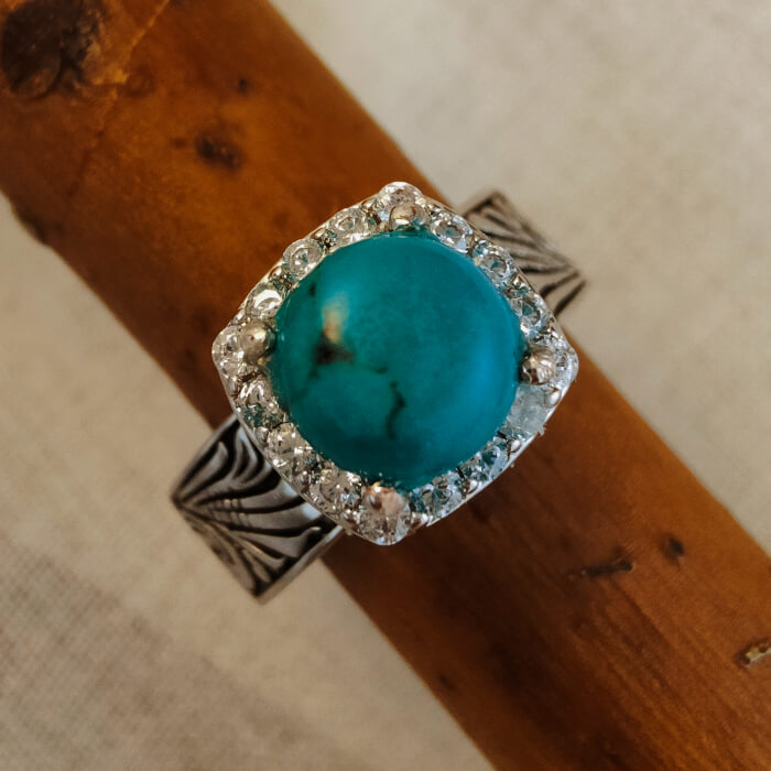 Flower engraved ring with turquoise center and diamond halo on black-silver band.