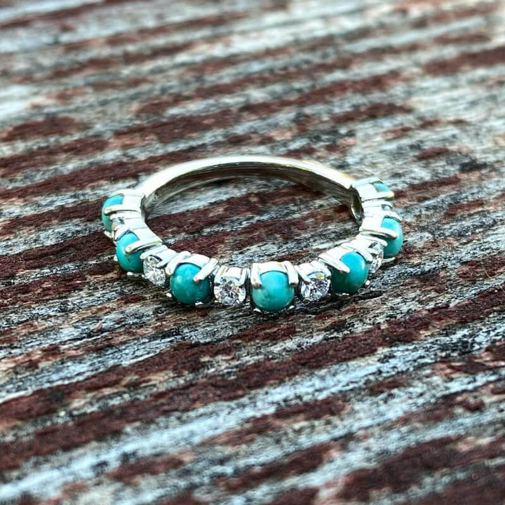 Silver band ring featuring turquoise and zircon stones on rustic wood.