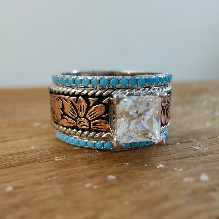 Rose gold ring with princess cut diamond and turquoise inlay, featuring floral engravings.