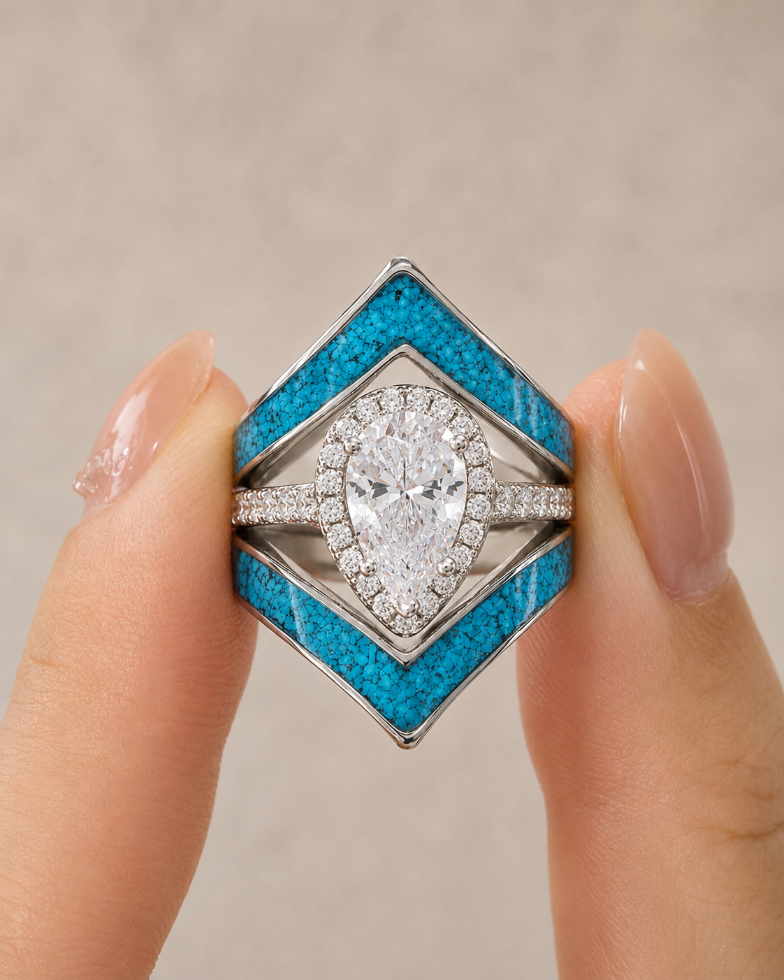 A close-up of a hand holding a geometric diamond-shaped ring with a large pear-cut center stone, surrounded by clear stones, and bright blue textured inlay panels on a silver-toned band.