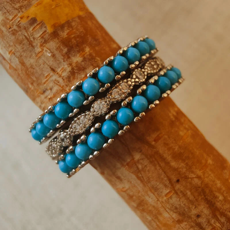 Three-piece turquoise bead and clear-stone ring stack angled on a wooden branch