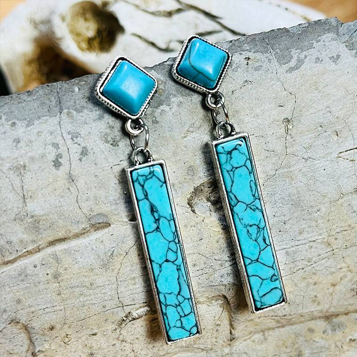 Rectangle turquoise drop earrings with silver frame and intricate design.