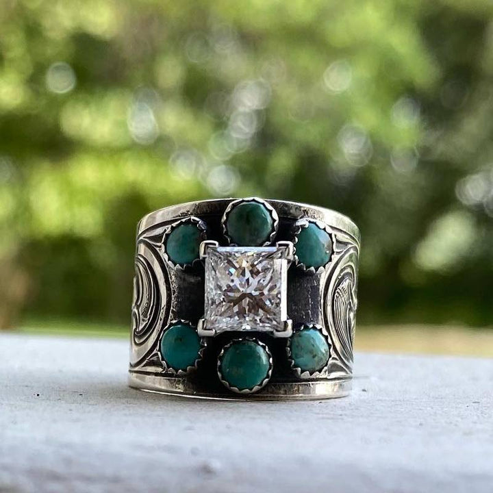 Wide band engagement ring with diamond center and turquoise accents, floral details.