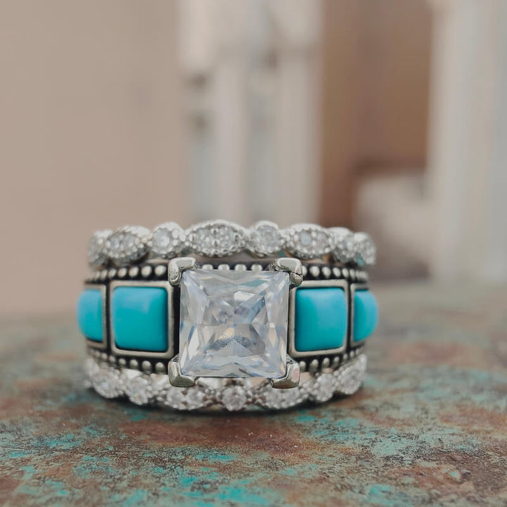 Vintage square turquoise and diamond ring with decorative band on textured surface.
