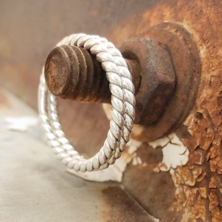 Sterling silver Western Twist Band Ring showcased on a rusty metal surface