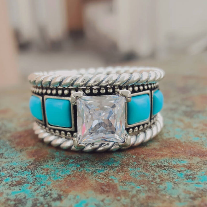 Vintage turquoise zircon ring with square cut stone and decorative band on rustic surface.