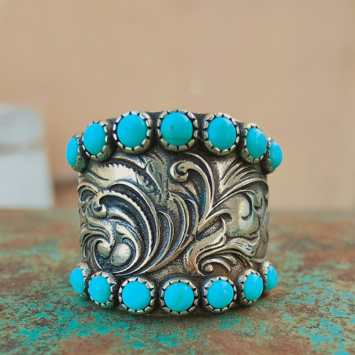 Silver cuff bracelet with intricate floral patterns and turquoise stones