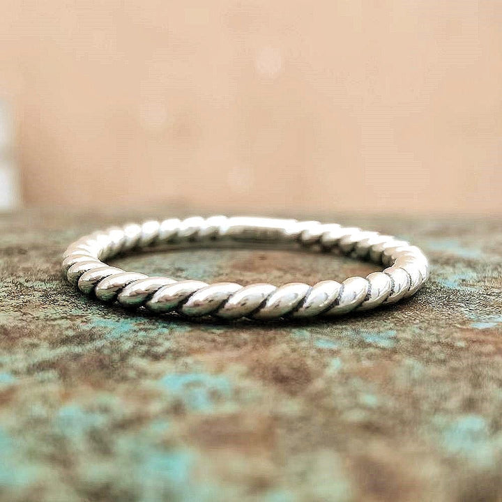 Twisted sterling silver band ring on a textured surface.