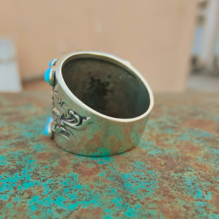 Side view of a silver cuff ring with floral engraving and turquoise accents